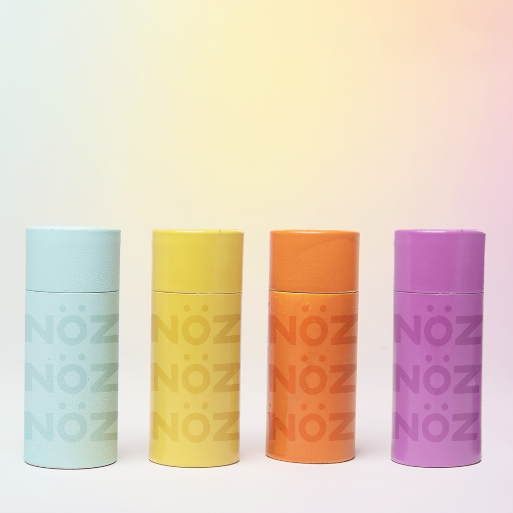 Set of 4 tinted Nöz reef safe sunscreens in the colors blue, yellow, orange, and purple with a yellow gradient background